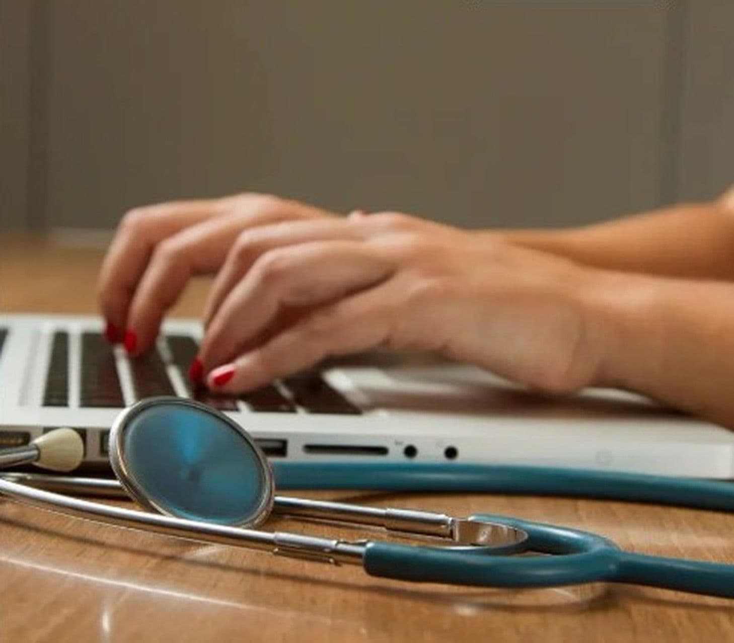 Hands at a laptop with a stethoscope resting on the desk